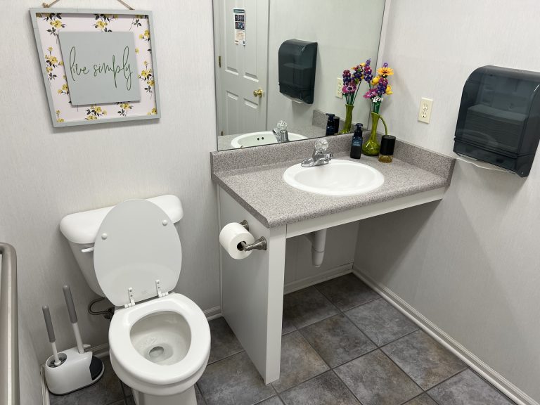 Large gender neutral restroom that is handicap accessible with a rail.