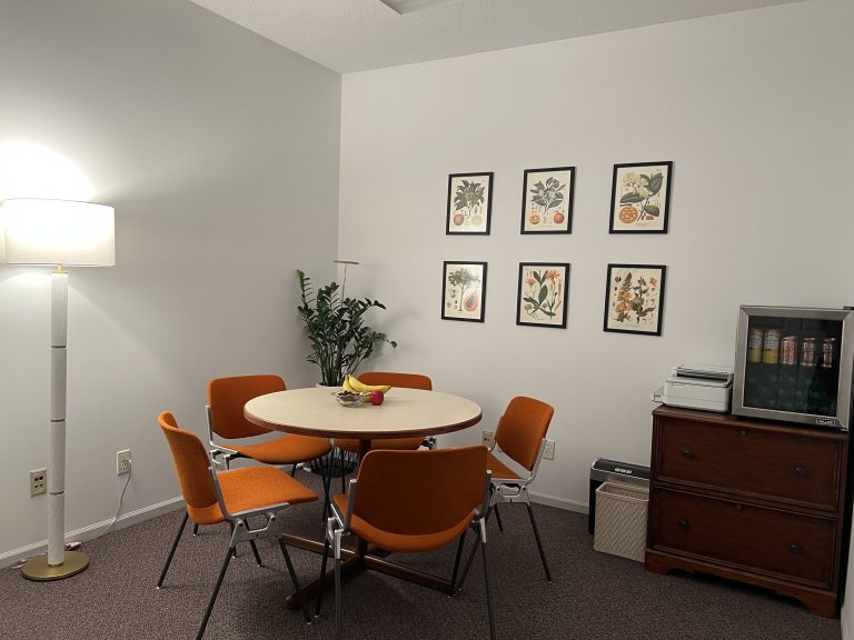 Break room that can be used as a waiting room with a large table, five chairs, snacks, and drinks.